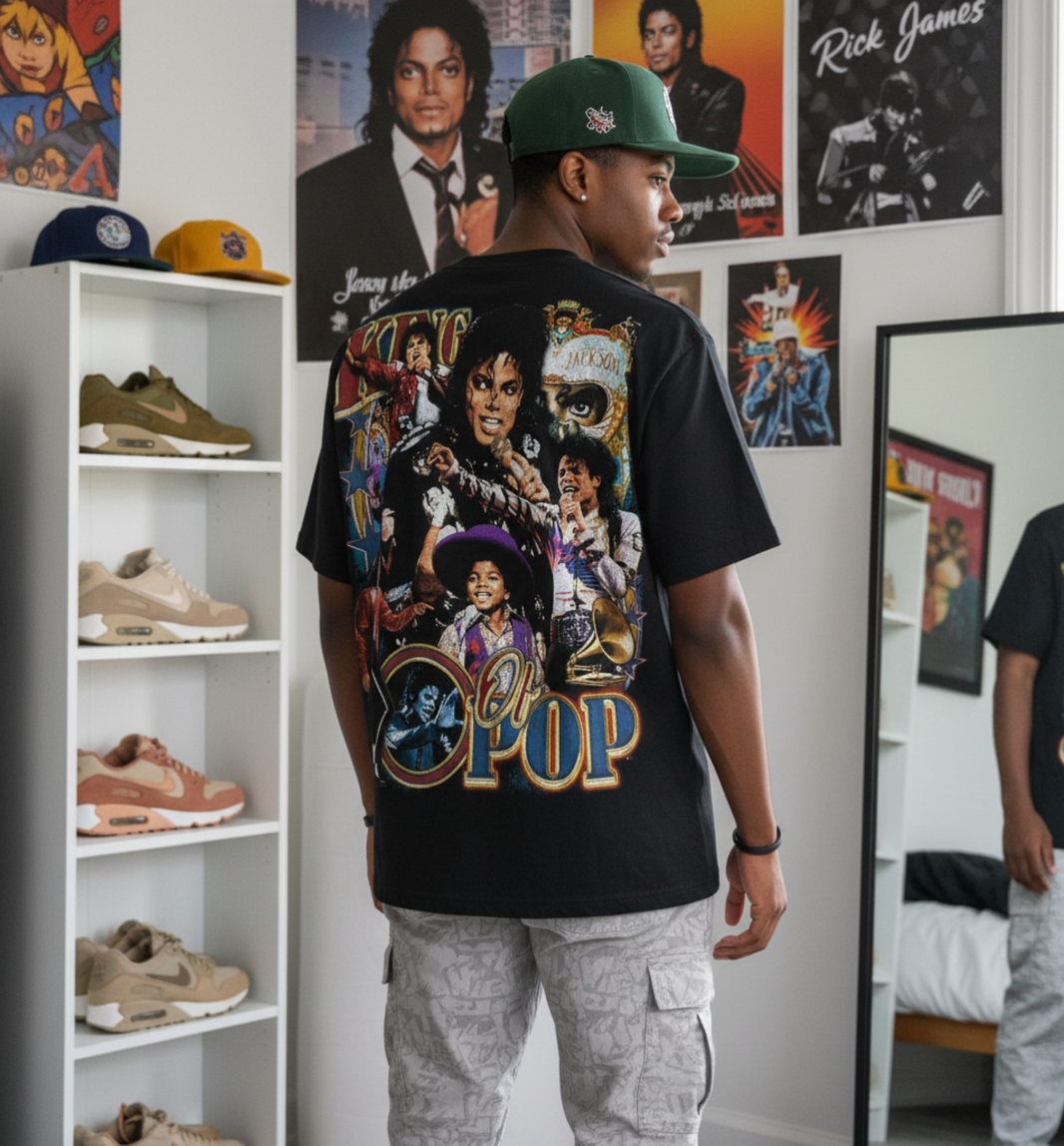 black male wearing a black graphic t-shirt with a colorful graphic design, standing in a room with shelves displaying shoes and posters on the wall.